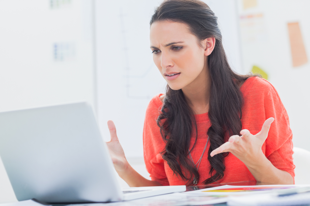 Annoyed designer gesturing in front of her laptop in her office Annoyed designer gesturing in front of her laptop in her office