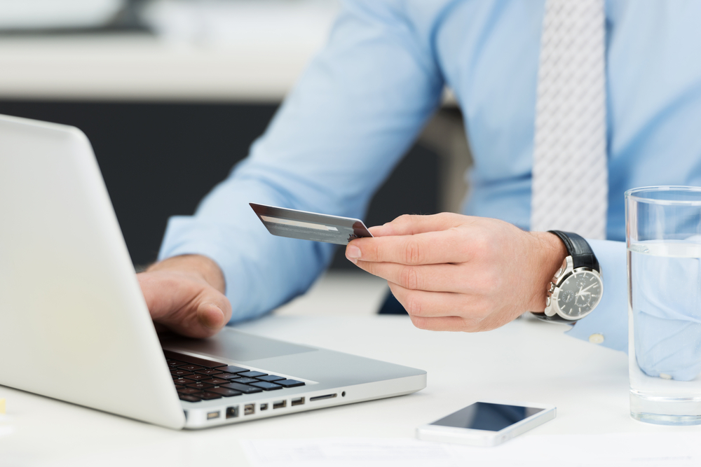 Businessman doing online banking, making a payment or purchasing goods on the internet entering his credit card details on a laptop, close up view of his hands-1 Businessman doing online banking, making a payment or purchasing goods on the internet entering his credit card details on a laptop, close up view of his hands-1