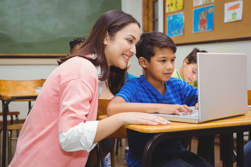 Happy teacher using laptop with student at the elementary school Happy teacher using laptop with student at the elementary school