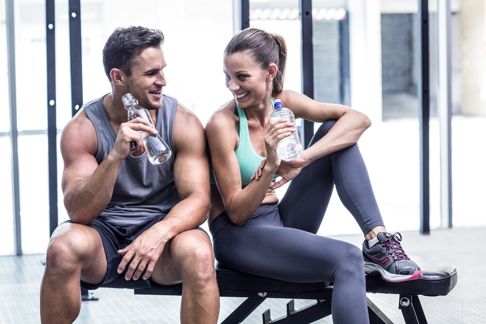 Muscular couple discussing on the bench and holding water bottle Muscular couple discussing on the bench and holding water bottle
