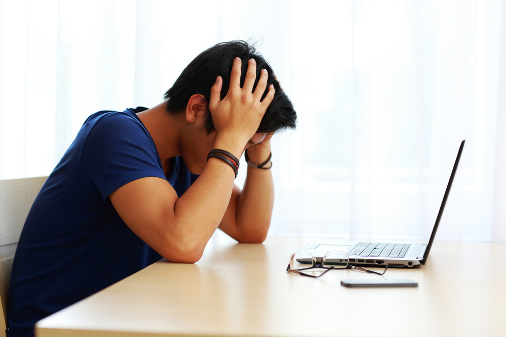 Young tired man sitting at the table with laptop at home Young tired man sitting at the table with laptop at home